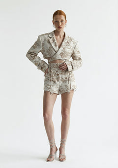Model wearing La Musa Savoy Shorts, high-waisted tapestry shorts in cream toile print with corset side lacing, styled with the matching Savoy Blazer