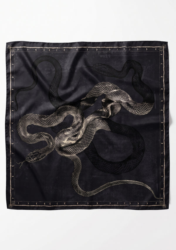 Temptation Scarf laid flat, a large square black silk scarf printed with intertwined ivory serpents inside a moon phase border