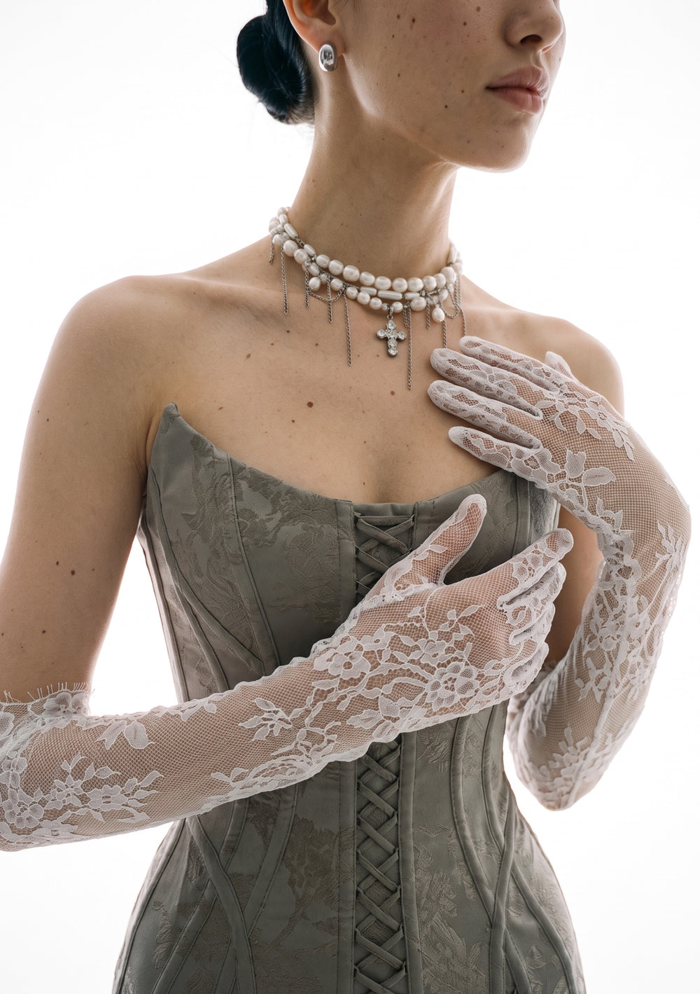 Close-up of the Etherea white lace opera gloves crossed at the chest, showing the sheer floral lace and eyelash-fringe edge