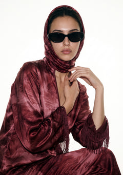 Model wearing the Crimson Dusk Scarf draped over the head and around the neck with the matching crimson landscape print set and black sunglasses