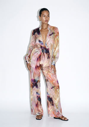 Blush pink floral silk pajama set on model, front view, tie-front shirt knotted at the waist over wide-leg trousers in an oversized lily print