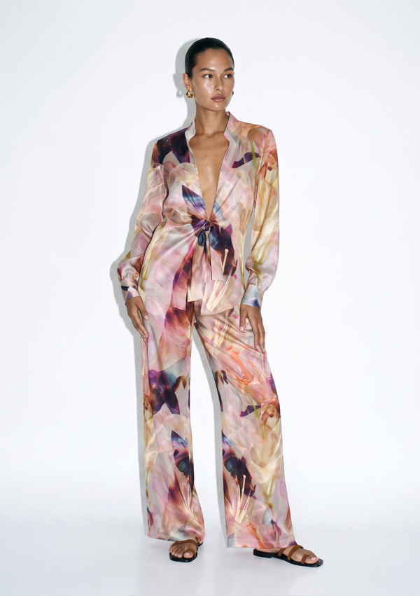 Blush pink floral silk pajama set on model, front view, tie-front shirt knotted at the waist over wide-leg trousers in an oversized lily print