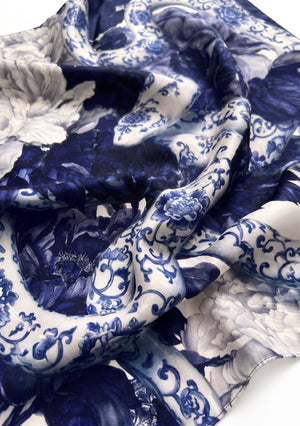 Close-up of the Mirage Peony Scarf silk, showing cobalt peonies and a porcelain-patterned serpent coil with a rolled edge