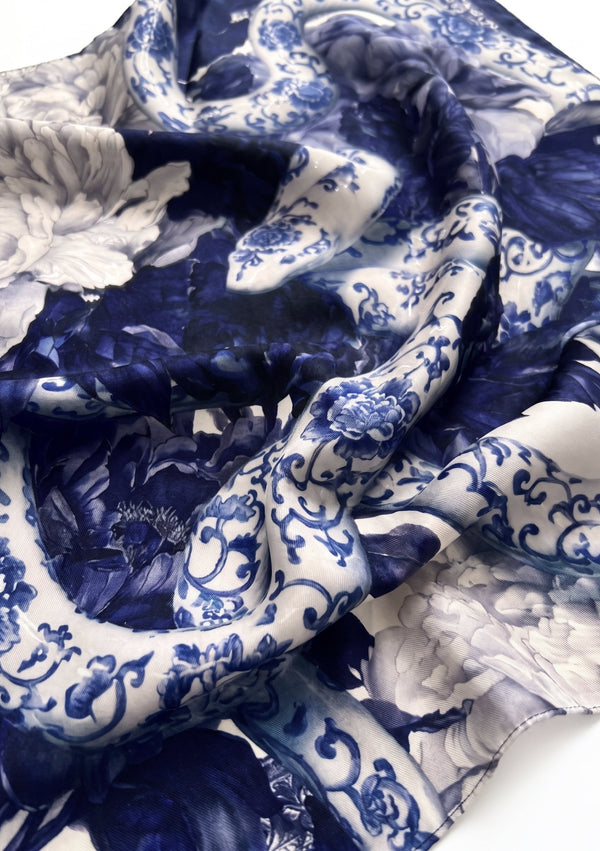Close-up of the Mirage Peony Scarf silk, showing cobalt peonies and a porcelain-patterned serpent coil with a rolled edge
