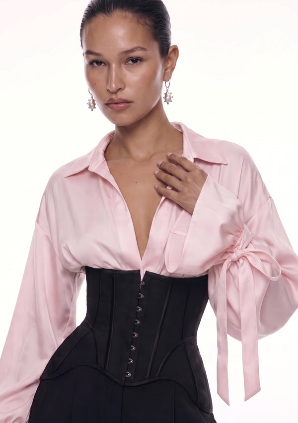 Close-up of the Petal Blouse in pink viscose, open collar and ribbon-tied cuffs, worn under a black busk-front corset.