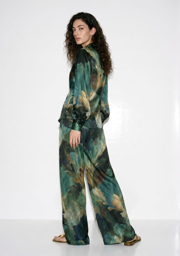 Sylvara silk set seen from behind, full length, showing the leaf print running across the shirt and the long fluid drape of the wide-leg trousers