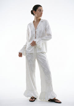 Ivory satin floral jacquard pajama set on model, tie-front shirt with ruffle cuffs and wide-leg trousers with ruffled hem