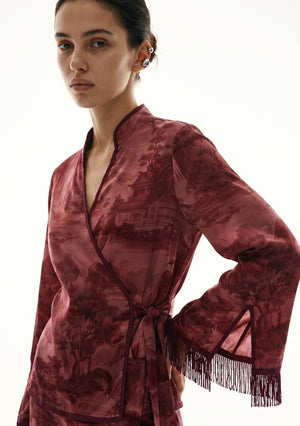 Crimson Dusk Set close view, hand on hip showing the wrap front, mandarin-style split collar, pagoda landscape print and the slit fringed cuff