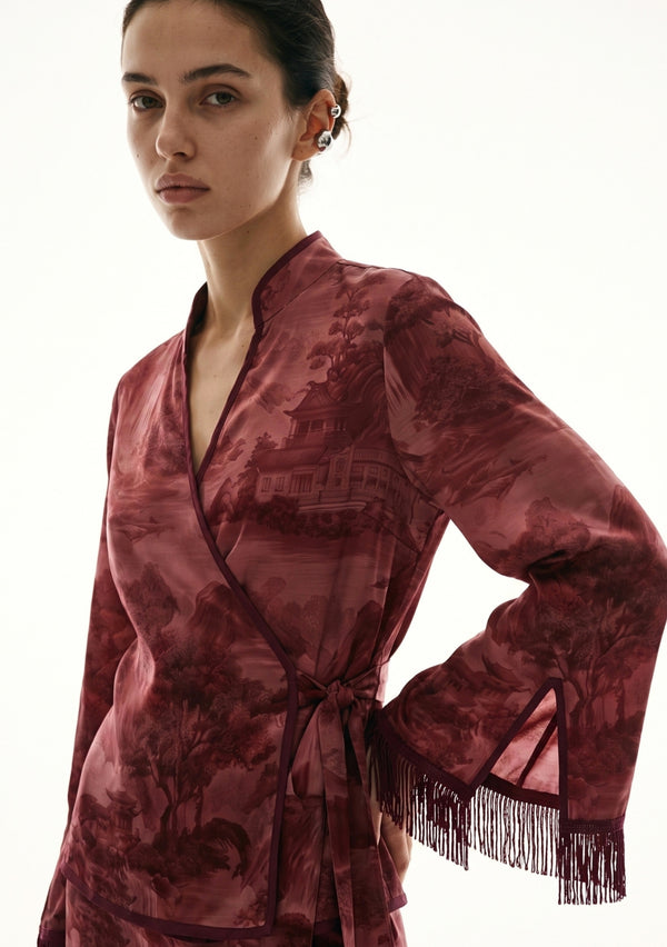 Crimson Dusk Set close view, hand on hip showing the wrap front, mandarin-style split collar, pagoda landscape print and the slit fringed cuff