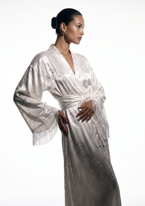 Moonveil robe three-quarter view, shawl collar crossing into a V above the tied sash, fringed cuff caught mid-movement