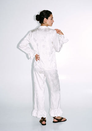 Ivory satin jacquard pajama set seen from behind, full length, showing the high-waisted wide-leg trousers and ruffled hem