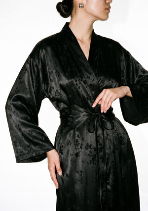 Waist-up view of the Tenebrae Robe, shawl collar, wide sleeves and belt tied in a bow at the waist, tonal floral jacquard catching the light