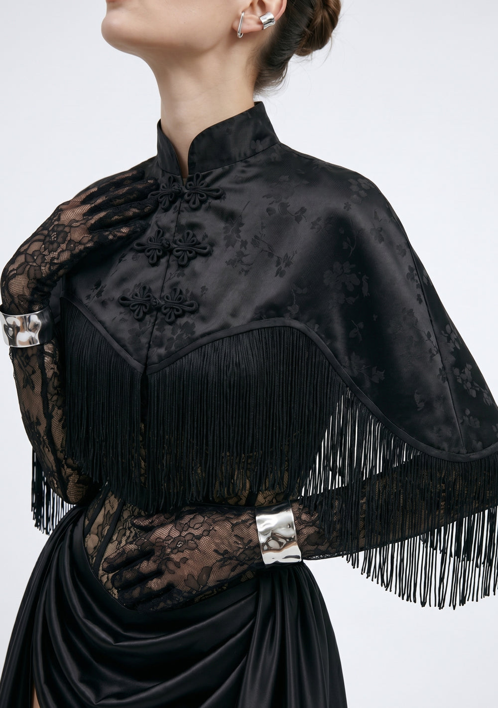 La Musa Baccara capelet close-up: satin jacquard floral weave, mandarin collar, frog closures and fringe