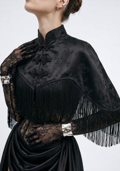 La Musa Baccara capelet close-up: satin jacquard floral weave, mandarin collar, frog closures and fringe