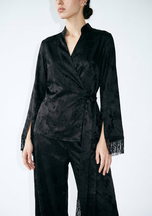 Front close-up of the Tenebrae wrap top, tonal floral black jacquard, deep V mandarin neckline, side-tie waist and fringed cuff slits