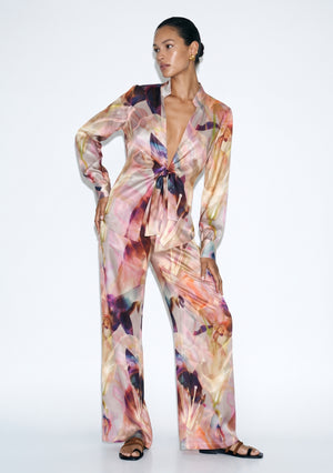 Blush pink lily print silk pajama set seen full length, tie-front shirt with long sleeves and high-rise wide-leg trousers with an open hem