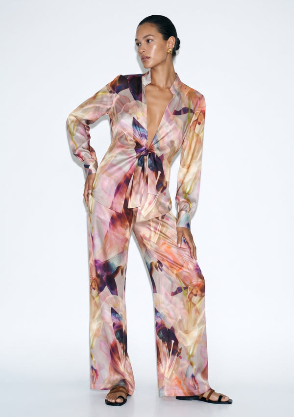 Blush pink lily print silk pajama set seen full length, tie-front shirt with long sleeves and high-rise wide-leg trousers with an open hem