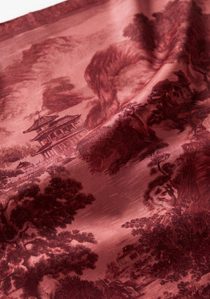 Fabric close up of the crimson printed silk showing the engraved pagoda, mountain and forest motif with a light catching sheen