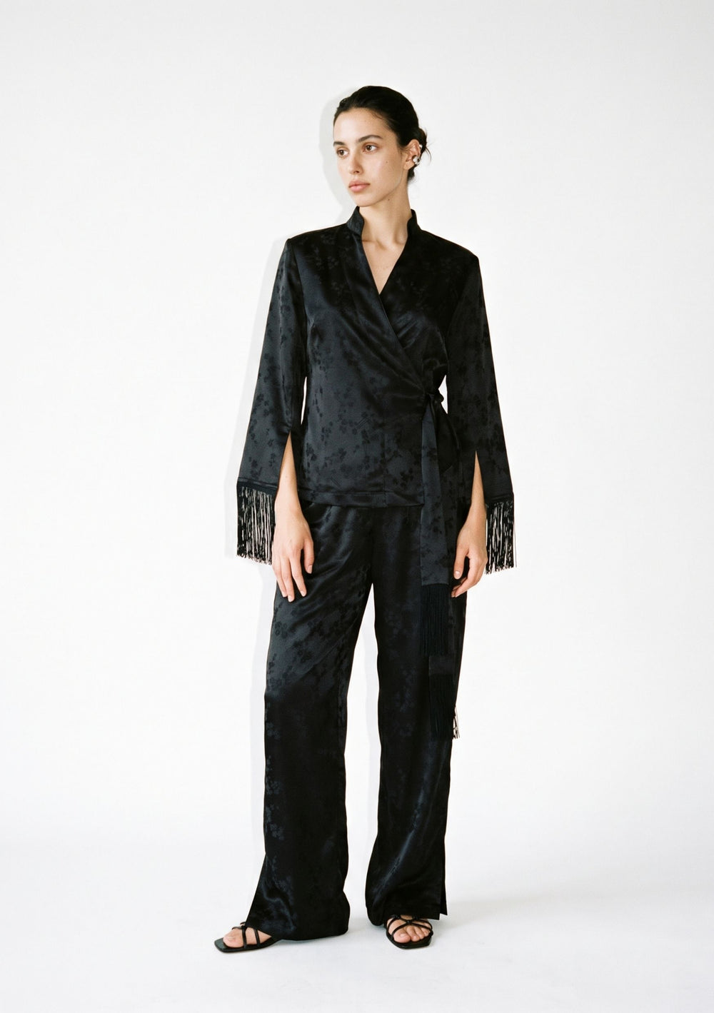 Tenebrae Set on model, full-length front view of the black jacquard wrap top with fringed cuffs and side sash, matching wide-leg trousers
