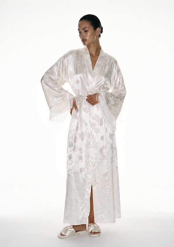 Moonveil ivory satin jacquard robe on model, floor-length wrap tied at the waist, long silk fringe falling from each wide sleeve