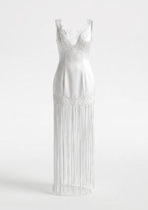 Lily Dress on a white background: deep V-neckline, floral lace at the neckline and hem band, long white fringe