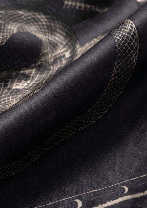 Macro close-up of the silk weave showing the fine snake scale print, ivory linework and the rolled edge of the scarf