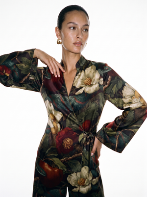 Close view of the Eden wrap top, showing the narrow stand collar, deep crossover V and a green serpent coiling across the cream magnolias