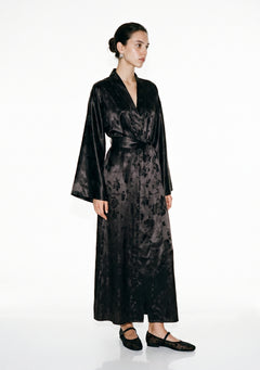 Tenebrae black satin jacquard robe on model, floor-length wrap silhouette tied with the wide belt, the long fringed sash hanging down the front