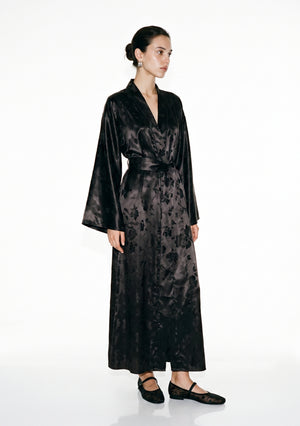 Tenebrae black satin jacquard robe on model, floor-length wrap silhouette tied with the wide belt, the long fringed sash hanging down the front