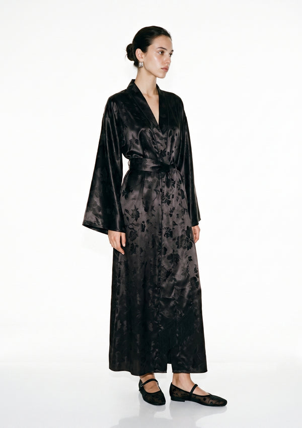 Tenebrae black satin jacquard robe on model, floor-length wrap silhouette tied with the wide belt, the long fringed sash hanging down the front