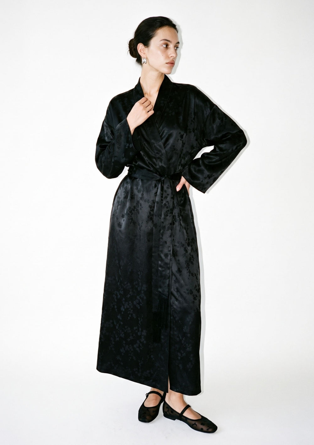 Tenebrae Robe on model, full-length front view of the floor-length black satin jacquard wrap robe with shawl collar, wide sleeves and fringed sash