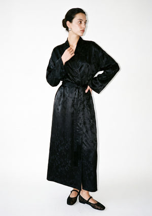 Tenebrae Robe on model, full-length front view of the floor-length black satin jacquard wrap robe with shawl collar, wide sleeves and fringed sash
