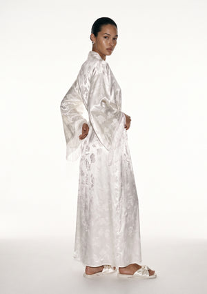 Moonveil robe in profile, floor-length ivory column with the fringed sleeve hanging along the body