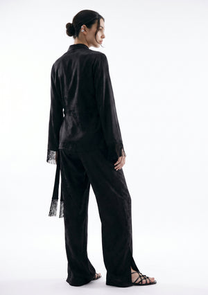 Back view of the Tenebrae Set, black jacquard top with fringed sleeve cuffs and long hanging sash over wide-leg trousers with side hem slits