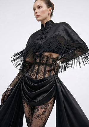 La Musa Baccara black satin-jacquard fringe capelet layered over the Baccara corset, three-quarter view