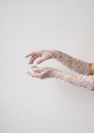 Both Etherea lace opera gloves on outstretched arms against a pale wall, showing the second-skin sheer fit and scalloped fringe edge