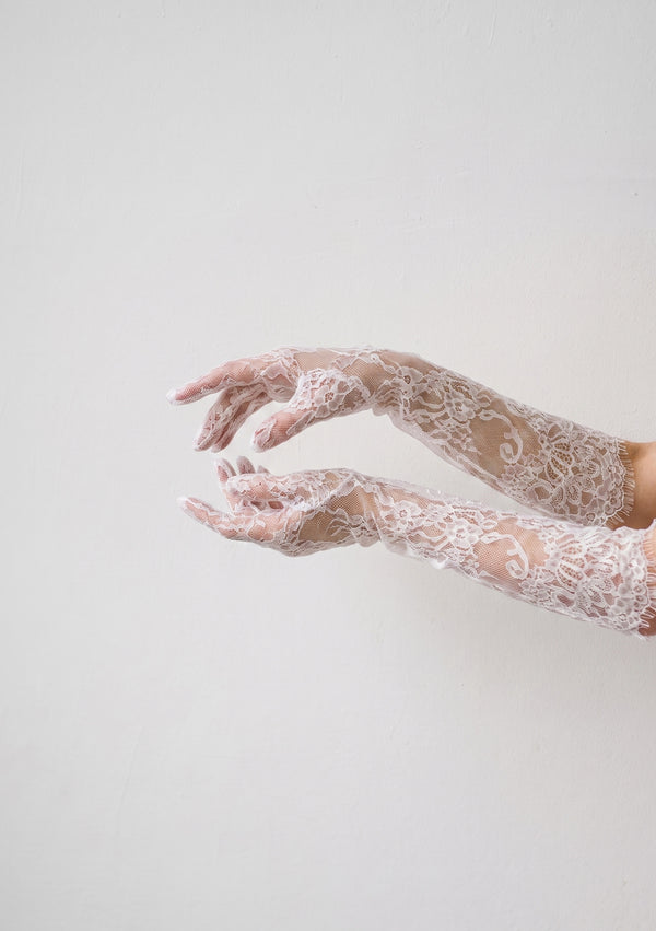 Both Etherea lace opera gloves on outstretched arms against a pale wall, showing the second-skin sheer fit and scalloped fringe edge