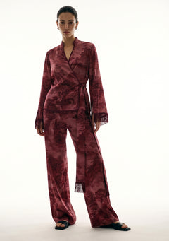 Crimson Dusk Set, burgundy printed satin pajama set, front view on model with the wrap top belted at the waist, fringed sleeve cuffs and wide-leg trousers worn with black flat sandals