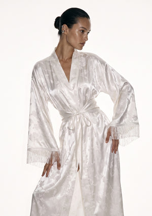 Detail of the Moonveil robe showing the woven floral on ivory satin and the long fringe trim at the sleeve