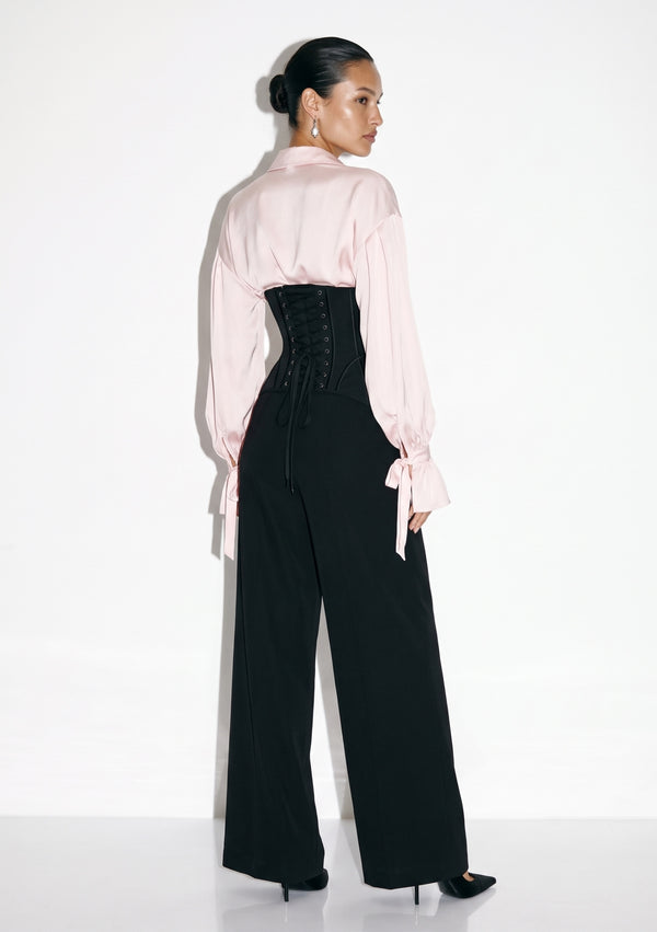 Back view of the Petal Blouse in pink viscose with full sleeves, worn with the black lace-up Elara Corset Trousers.