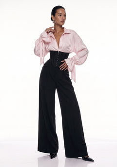 Petal Blouse in pink viscose with voluminous sleeves and bow-tied cuffs, worn with the black Elara Corset Trousers, front view.