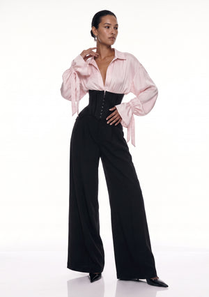 Petal Blouse in pink viscose with voluminous sleeves and bow-tied cuffs, worn with the black Elara Corset Trousers, front view.