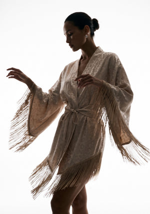 Feline robe with both arms raised, the fringed sleeves opening wide against the light