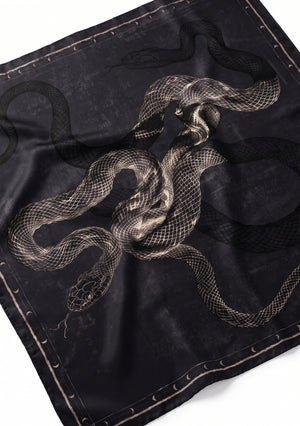 Angled flat view of the black silk scarf showing the engraved snake print artwork and crescent moon border in close detail