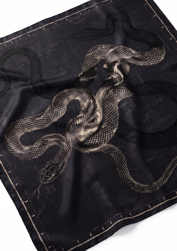 Angled flat view of the black silk scarf showing the engraved snake print artwork and crescent moon border in close detail