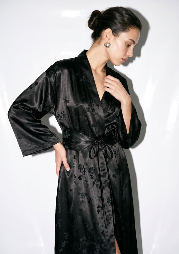 Side view of the Tenebrae Robe on model, black satin jacquard wrap robe belted at the waist with the wide sleeve falling loose
