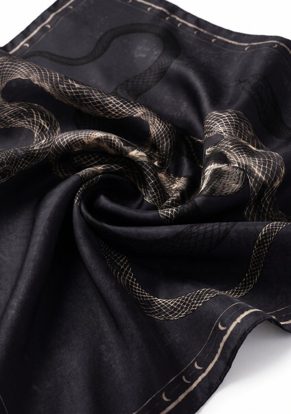 The Temptation Scarf swirled and draped, showing the fluid silk drape and the ivory serpent print against the smoky black ground