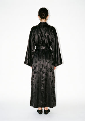 Full back view of the Tenebrae robe on model, floor-length with the belt fastened behind and the jacquard floral across the back