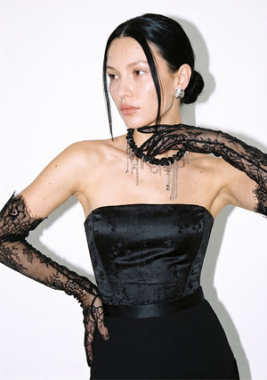 Side view of the strapless Spell Corset in black satin jacquard, with lace opera gloves and a statement necklace.