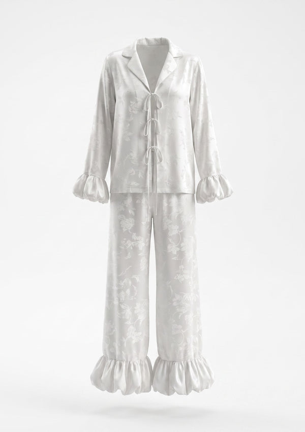 Moonveil ivory satin pajama set shown flat, showing the three satin front ties, notched collar and gathered ruffle cuffs and hem